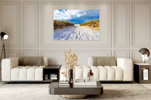 A modern living room with two white sofas, a black coffee table, neutral decor, and a stunning wall art of a sandy beach path under a blue sky, beautifully displayed as Chromaluxe Metal Prints. Prints 4 You