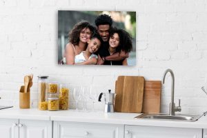A white kitchen with jars of pasta, wine glasses, and cutting boards sits below a photo on the wall—printed as a Single ChromaLuxe Indoor Metal Photo Print—showing four people smiling and embracing outdoors. Prints 4 You