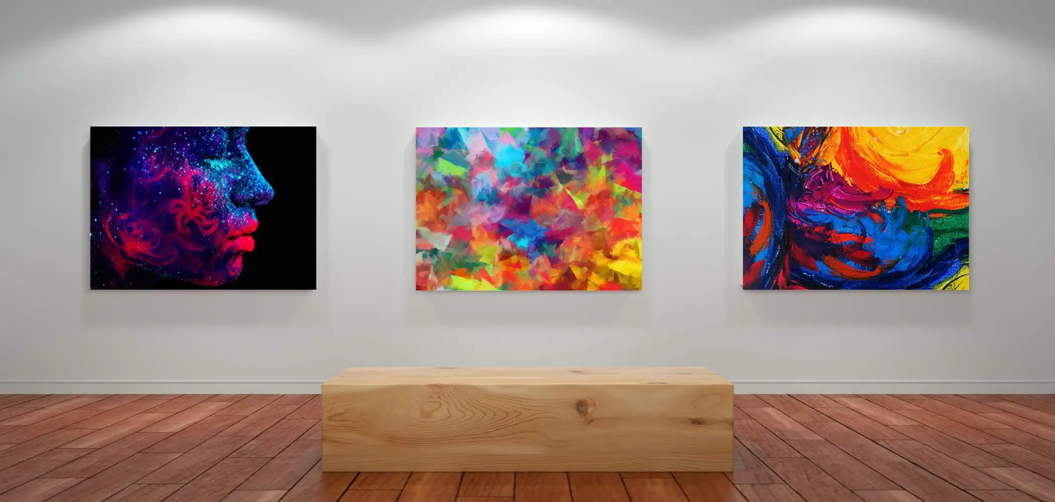 Three colorful abstract paintings hang on a white gallery wall above a wooden bench on a polished wooden floor under spotlights. The left piece features a vibrant face, the center a multicolor mosaic, and the right swirling bold hues. A metal photo print made by Prints 4 You